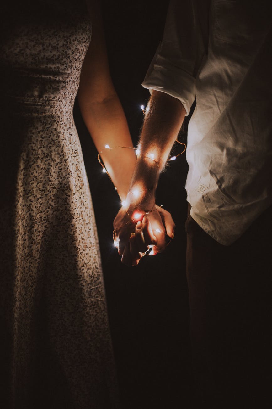 man and woman holding each others hand wrapped with string lights